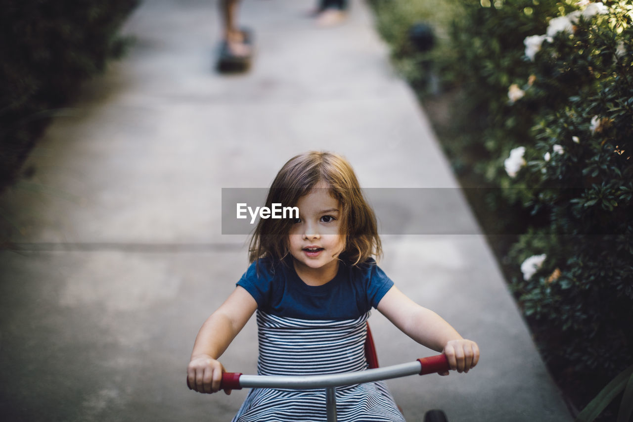 Girl riding tricycle on footpath