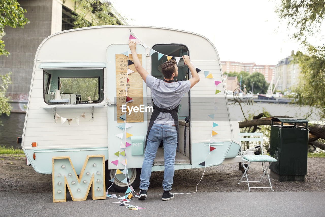 Full length rear view of male owner hanging bunting on food truck