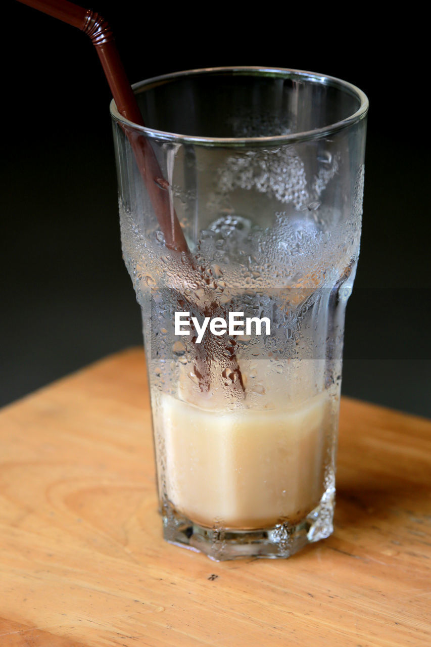 Close-up of half full iced coffee glass on wooden table