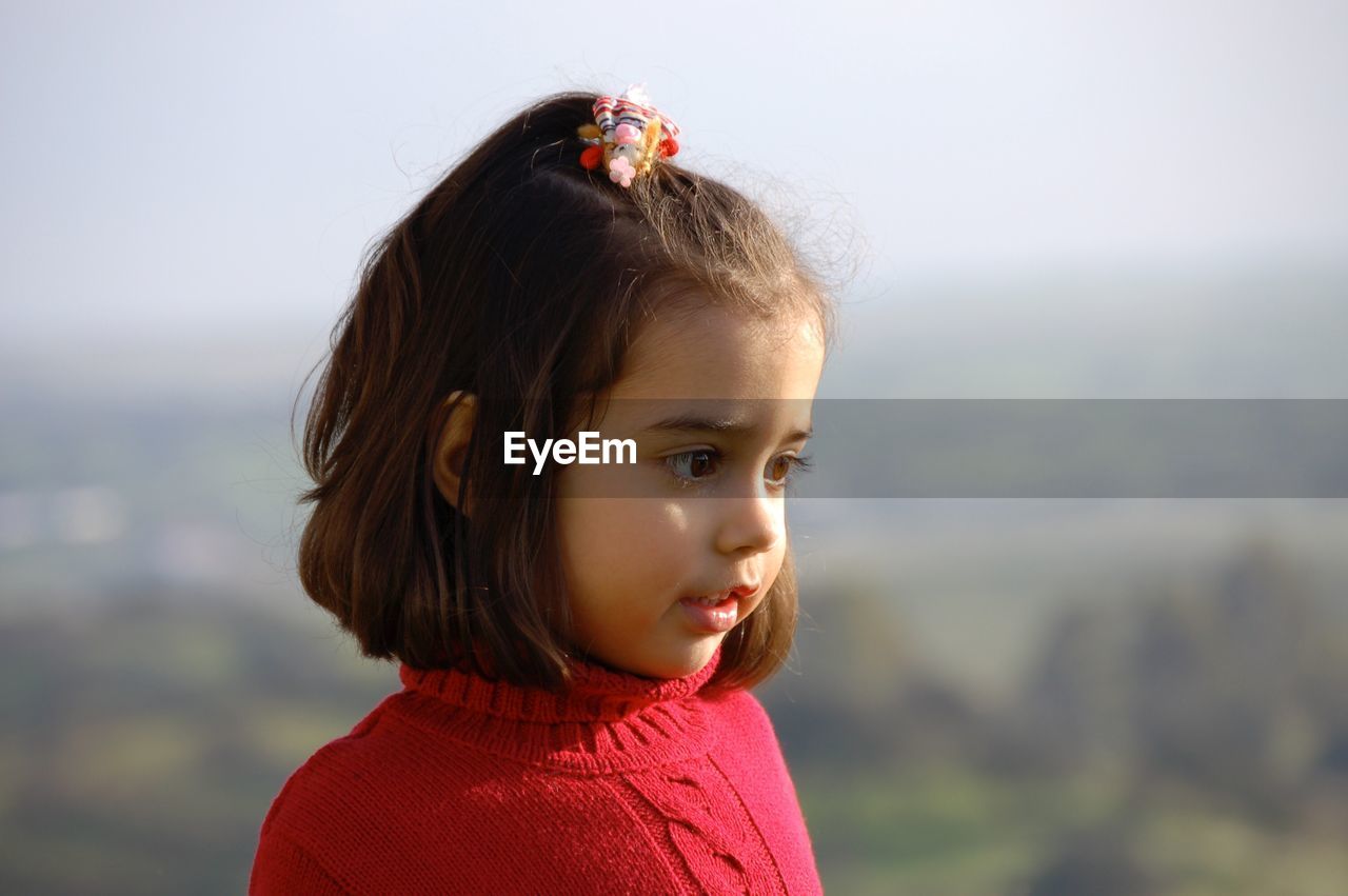 Cute girl looking away while standing against sky