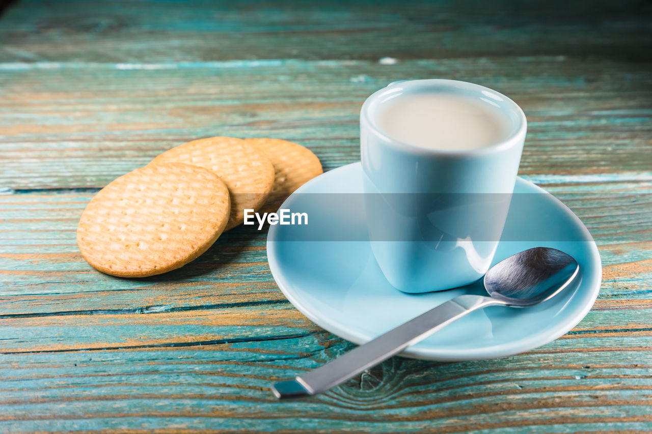 food and drink, food, drink, cup, crockery, refreshment, mug, spoon, eating utensil, kitchen utensil, coffee, wood, coffee cup, table, baked, freshness, breakfast, saucer, tableware, meal, hot drink, healthy eating, no people, indoors, wellbeing, dessert, plate, dairy, studio shot, teaspoon, morning, blue, still life, high angle view, milk, bread, sweet food