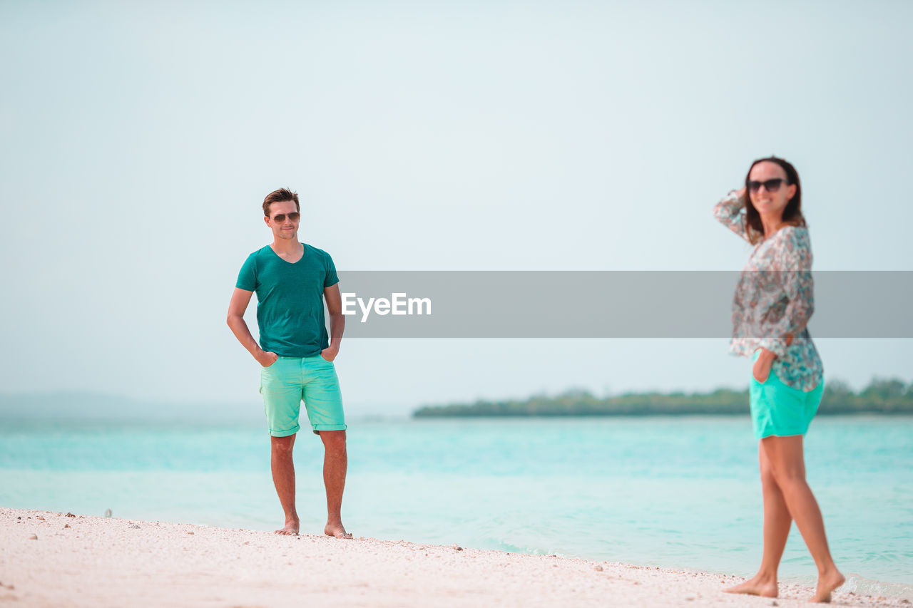 Full length of young man standing on beach against clear sky