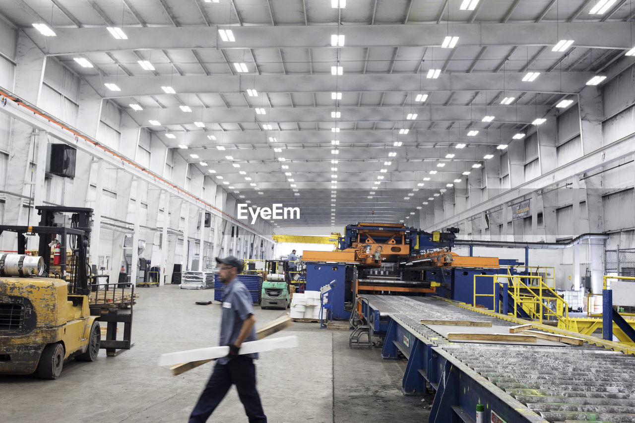 Side view of worker carrying wood while walking in steel industry factory