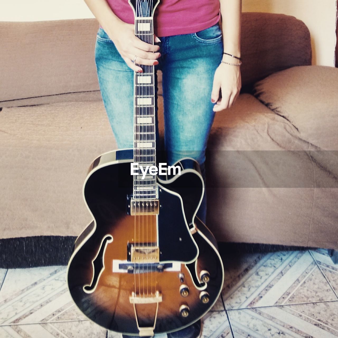 MIDSECTION OF WOMAN PLAYING GUITAR ON SOFA