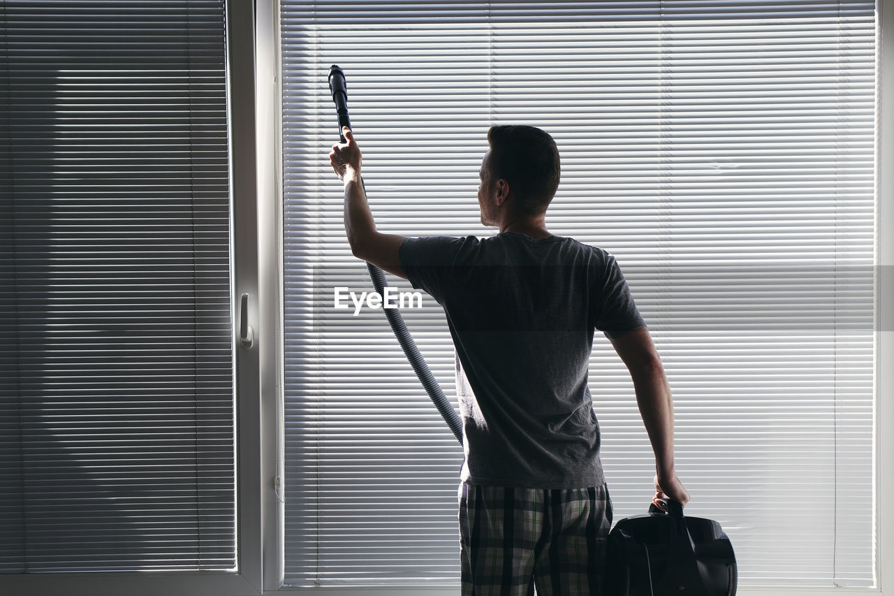 Rear view of man cleaning window at home