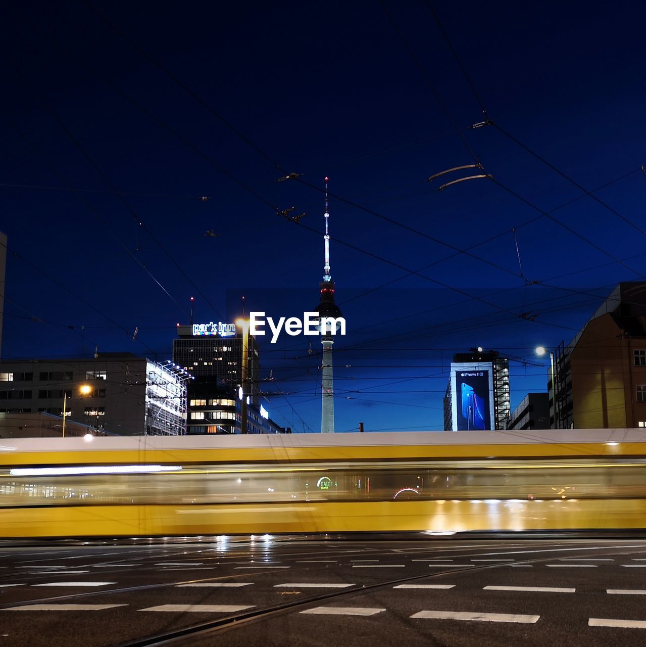 LIGHT TRAILS ON ROAD AGAINST ILLUMINATED BUILDINGS AT NIGHT