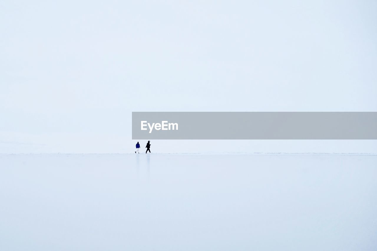 Men walking on frozen lake against clear sky