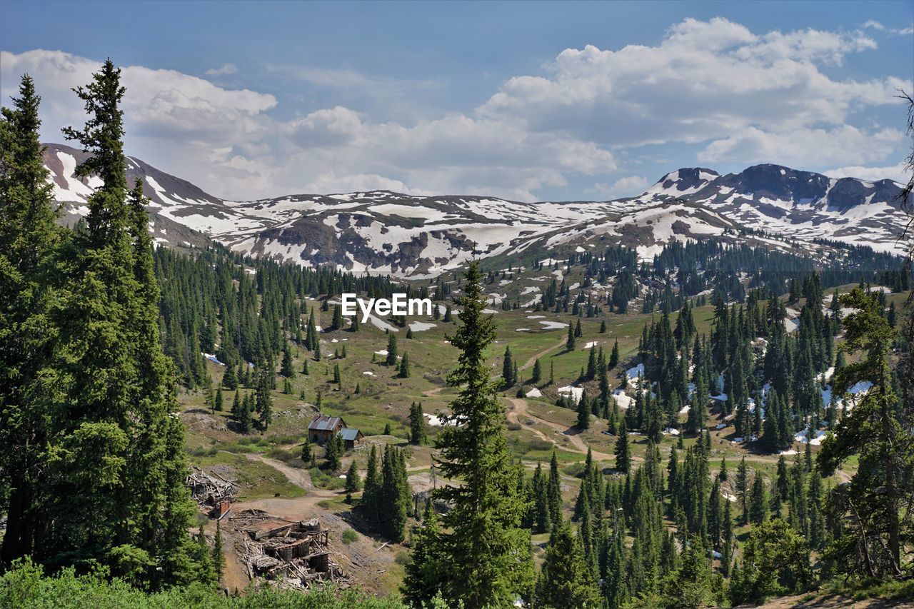 Panoramic view of trees, mountains and log buildings against sky