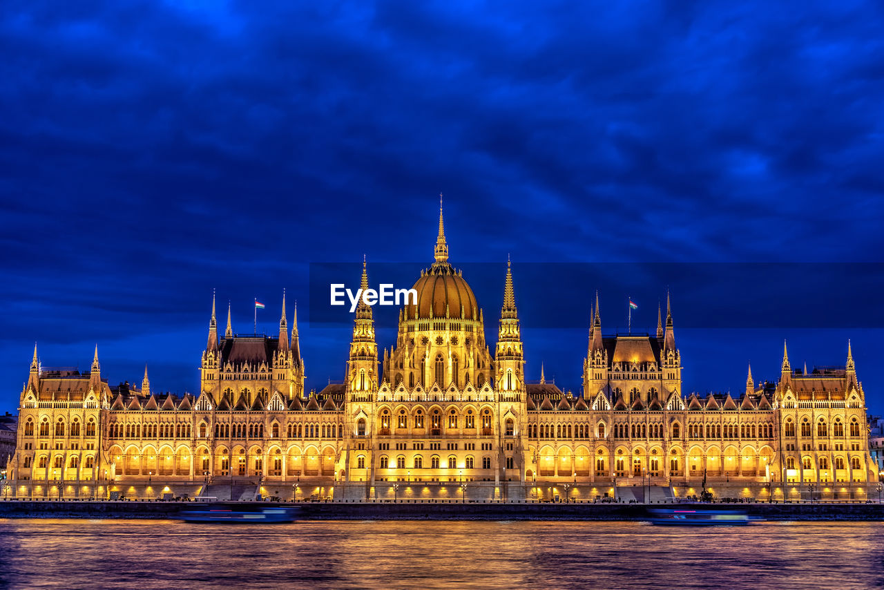 Illuminated hungarian parliament building by danube river in city at dusk