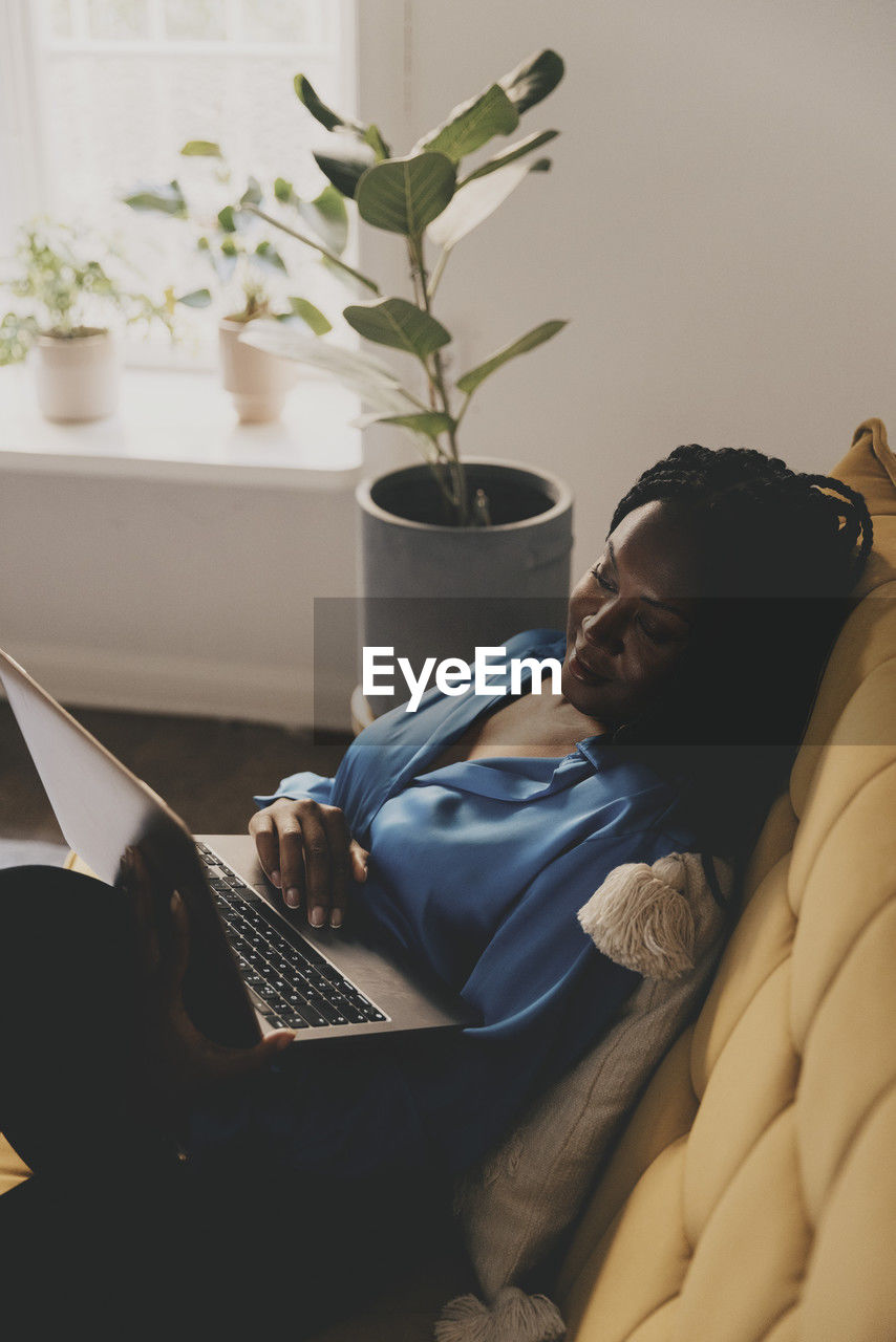 Businesswoman working on laptop while reclining on sofa at home