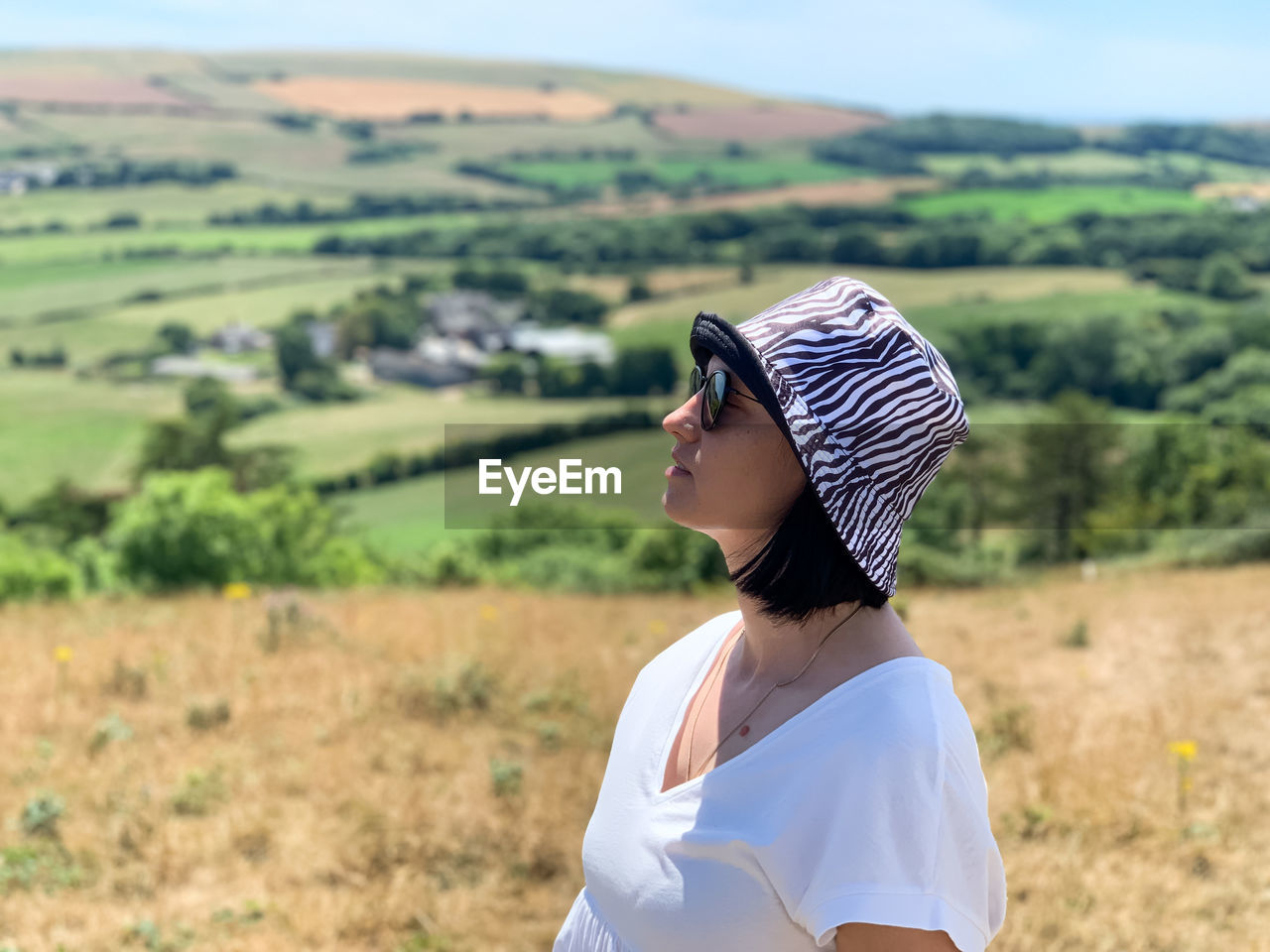 Portrait of young woman in panama hat with field on background. side view of young woman in white t