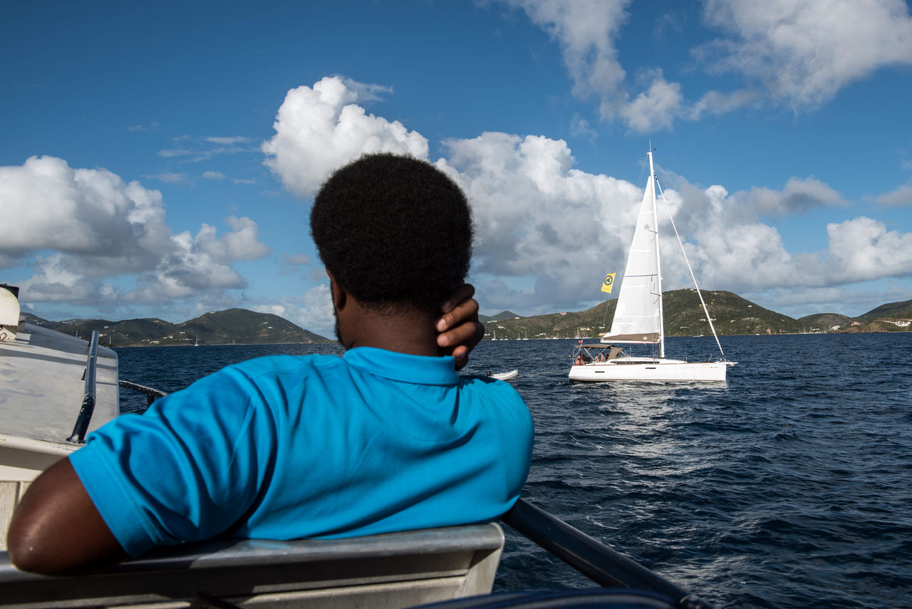 REAR VIEW OF MEN SITTING ON SAILBOAT IN SEA