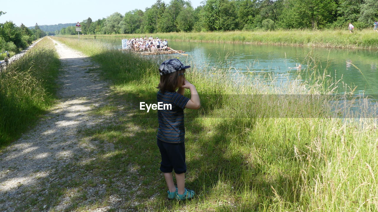 plant, water, nature, grass, one person, full length, day, waterway, leisure activity, lifestyles, growth, casual clothing, beauty in nature, rear view, green, lake, childhood, child, men, women, tree, land, adult, outdoors, standing, field, sunlight, wetland, tranquility, female, landscape, hat, scenics - nature, non-urban scene, sky, meadow, rural scene, walking, activity