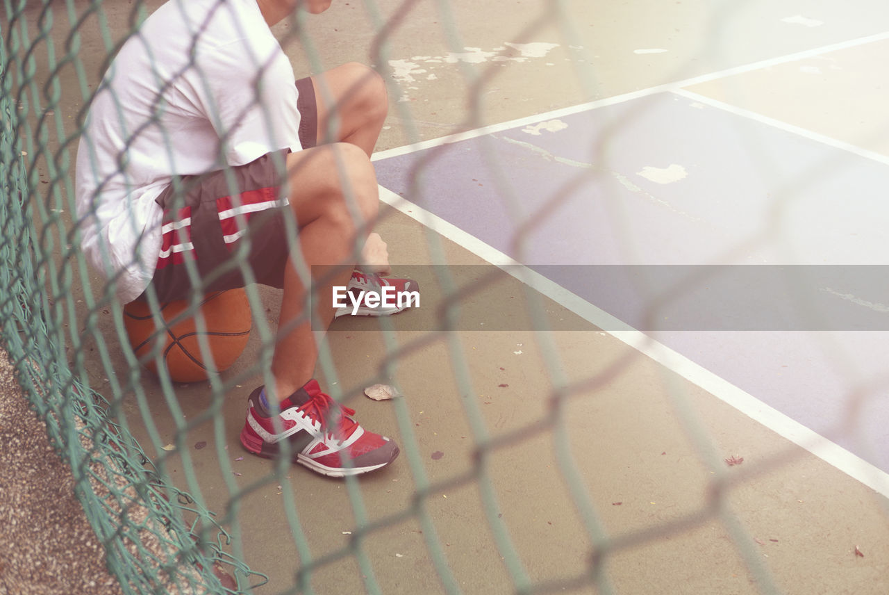 Low section of man sitting on basketball