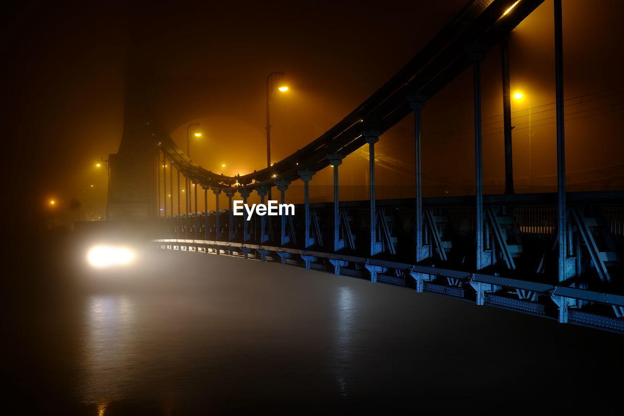 Illuminated bridge over river against sky at night