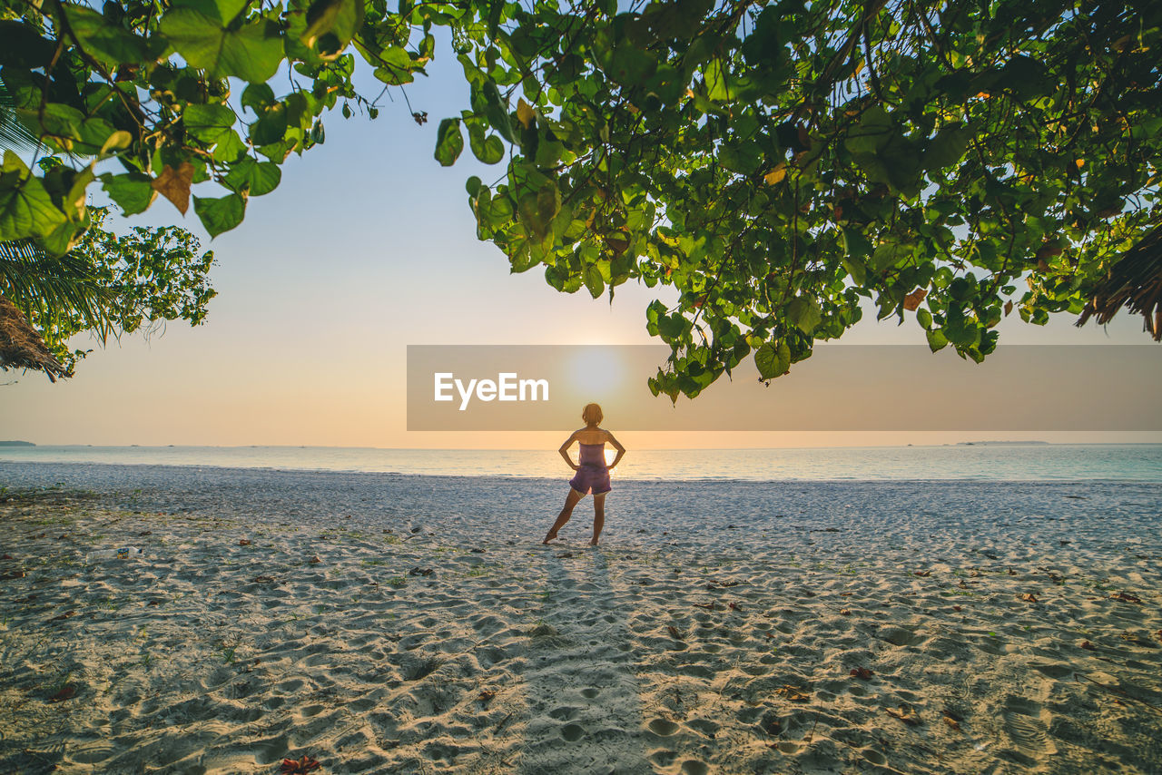 Woman standing at beach against sky during sunset