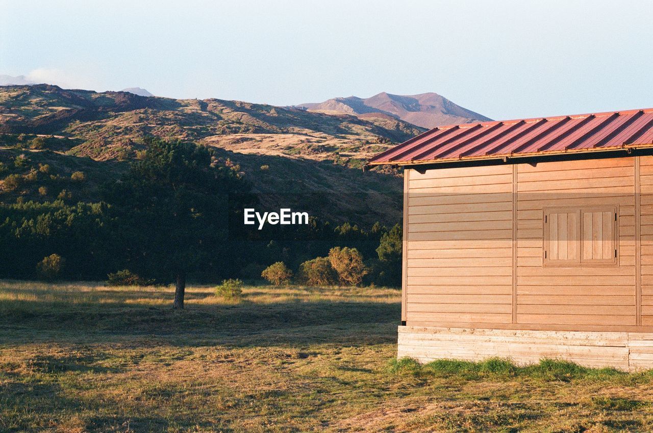 House on field by mountains against clear sky