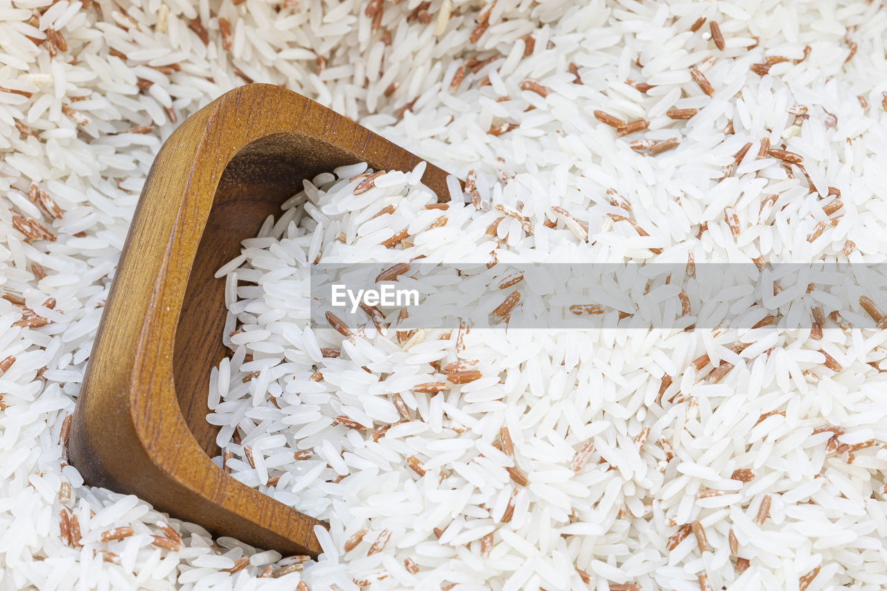 Close up a wooden cup on white rice mix with red rice background.