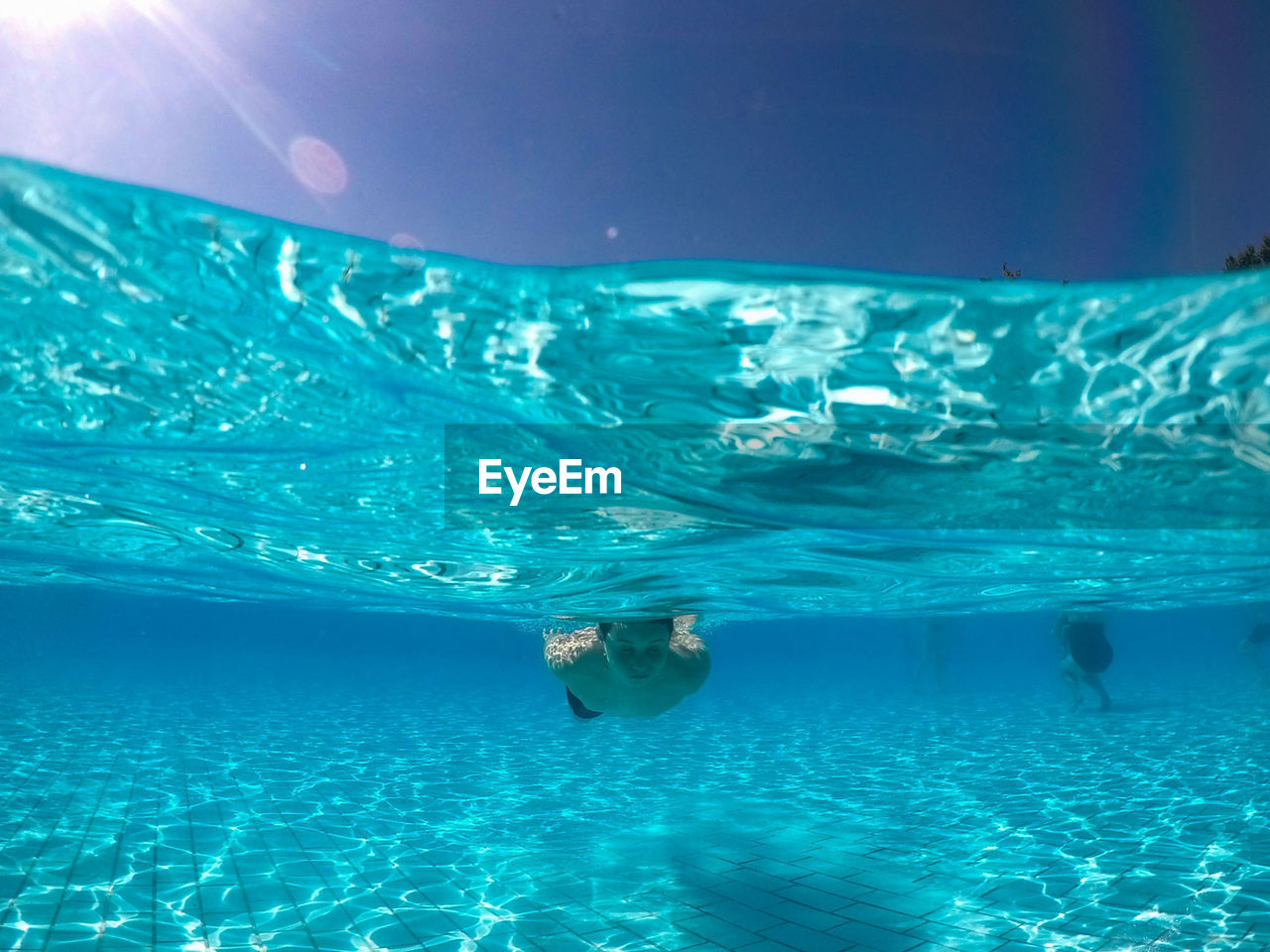 Water surface shot of boy swimming in pool during sunny day