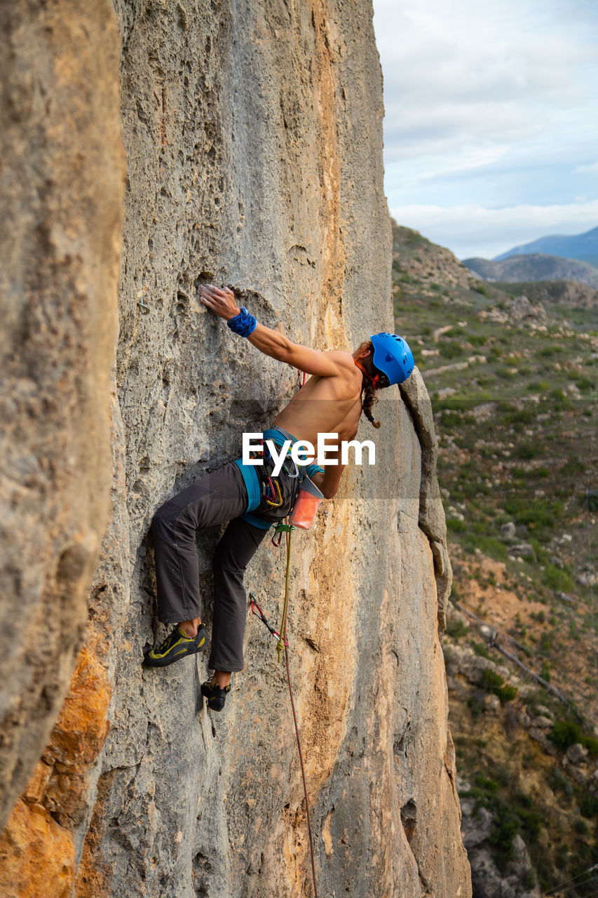 Shirtless man rock climbing against sky