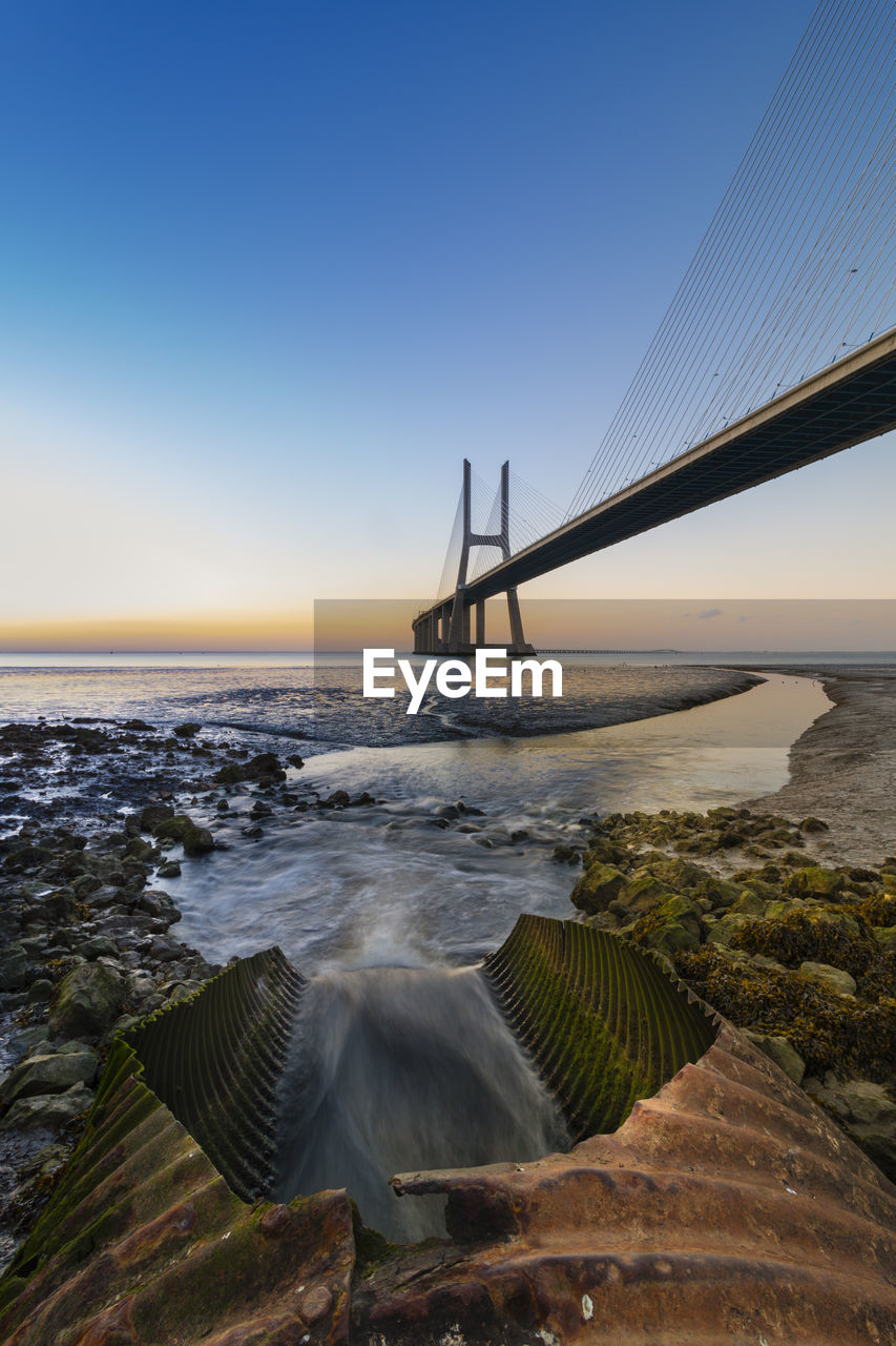 Cable-stayed bridge over river during sunset