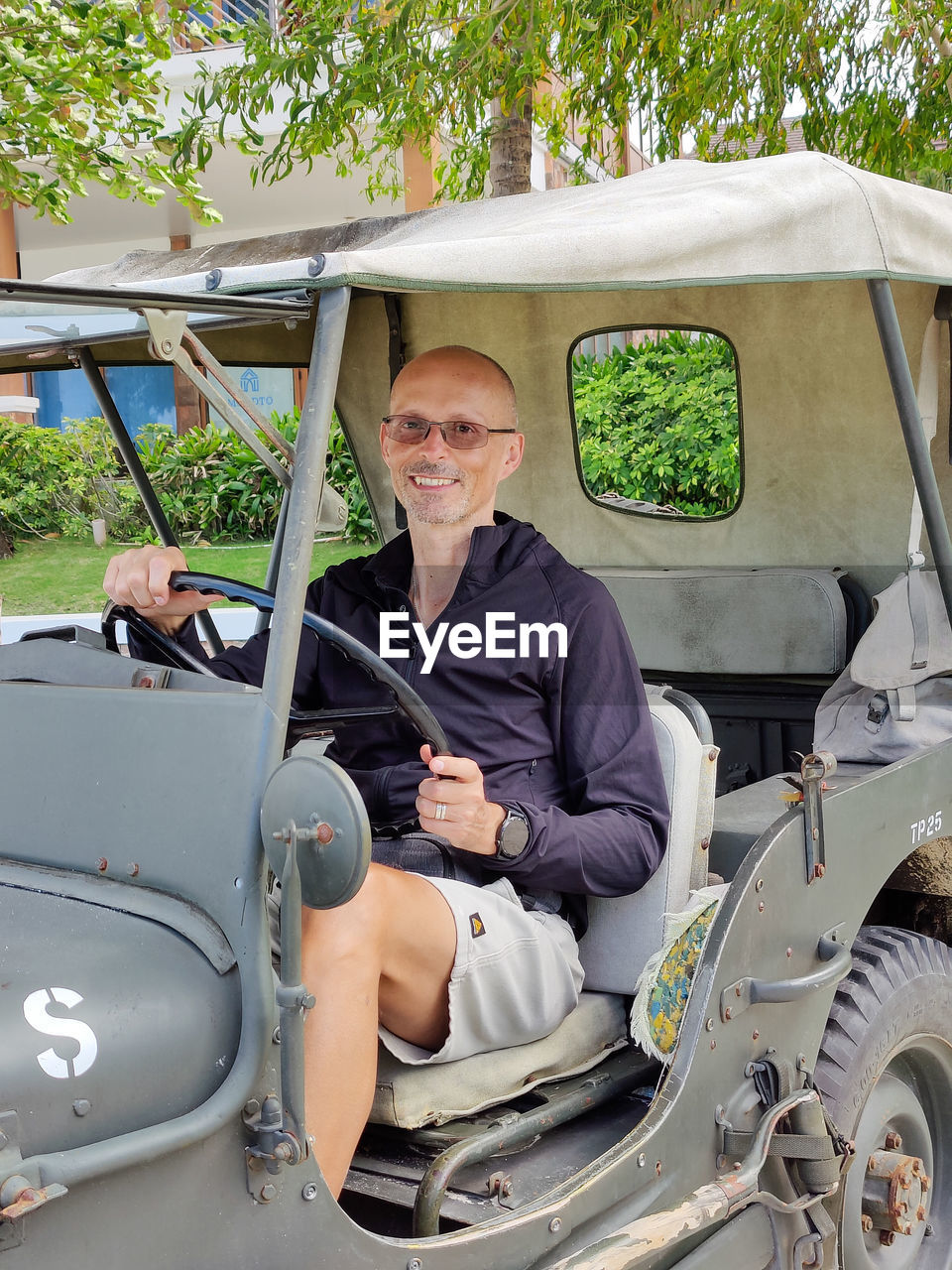 transportation, adult, mode of transportation, one person, men, portrait, car, looking at camera, vehicle, senior adult, golf cart, motor vehicle, day, mature adult, seniors, sitting, smiling, leisure activity, driving, casual clothing, land vehicle, glasses, lifestyles, nature, outdoors, emotion, travel, retirement, front view, happiness, full length, plant, gray hair, three quarter length