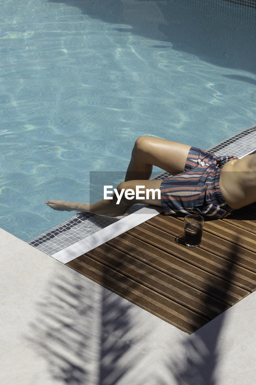 Vertical view of unrecognizable young man on striped swimsuit under a palmtree leaf shadow