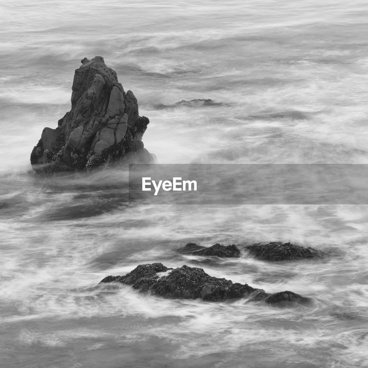 Black and white long exposure of waves around sea stack.