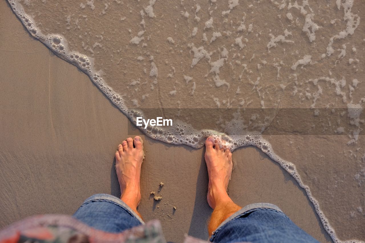 Low section of man standing on wet shore