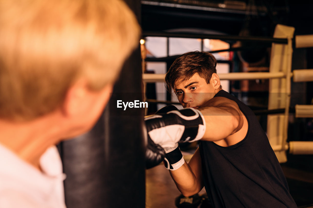 Instructor standing by boxer punching bag in boxing ring