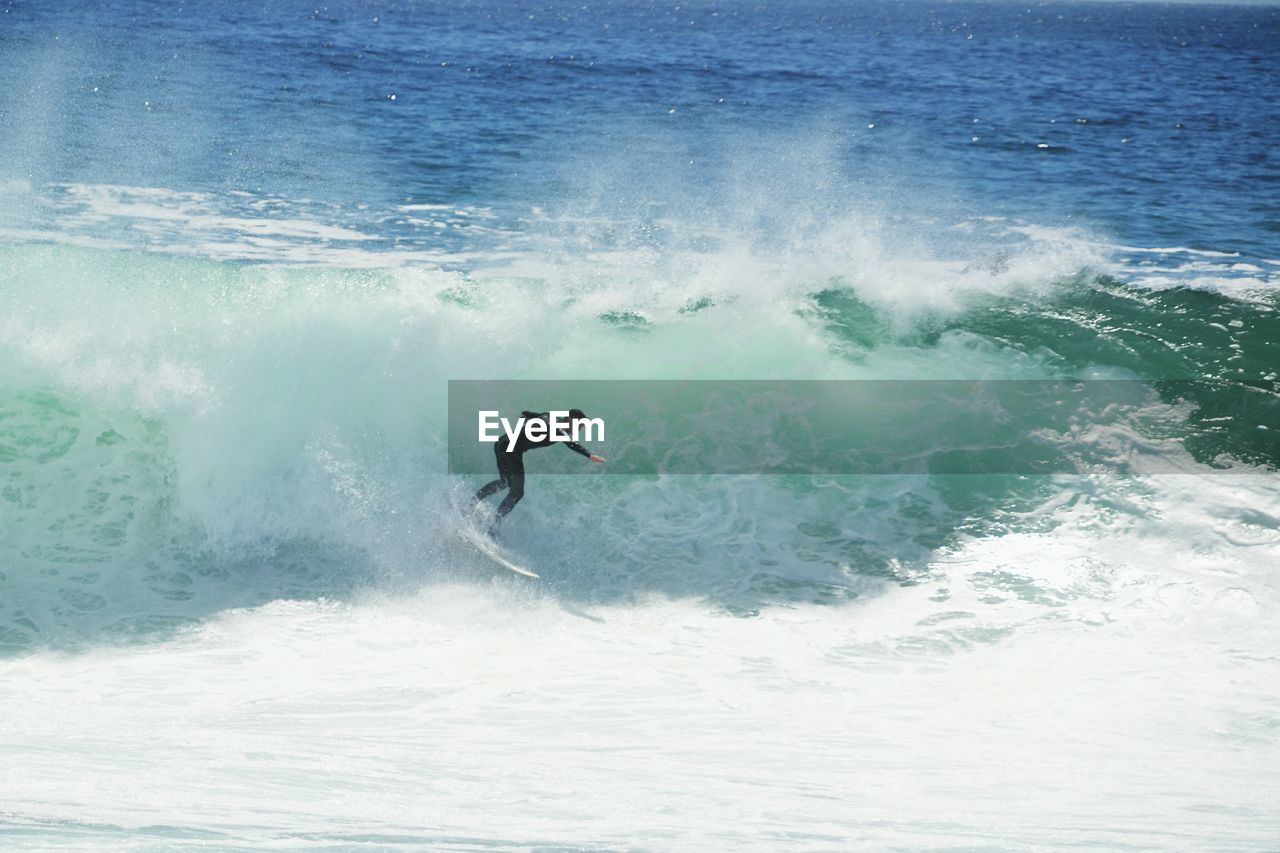 Side view of man surfboarding on wave in sea