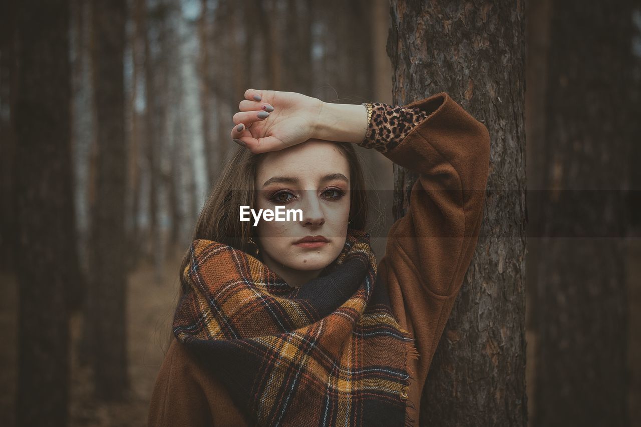 Portrait of young woman standing against tree trunk during winter