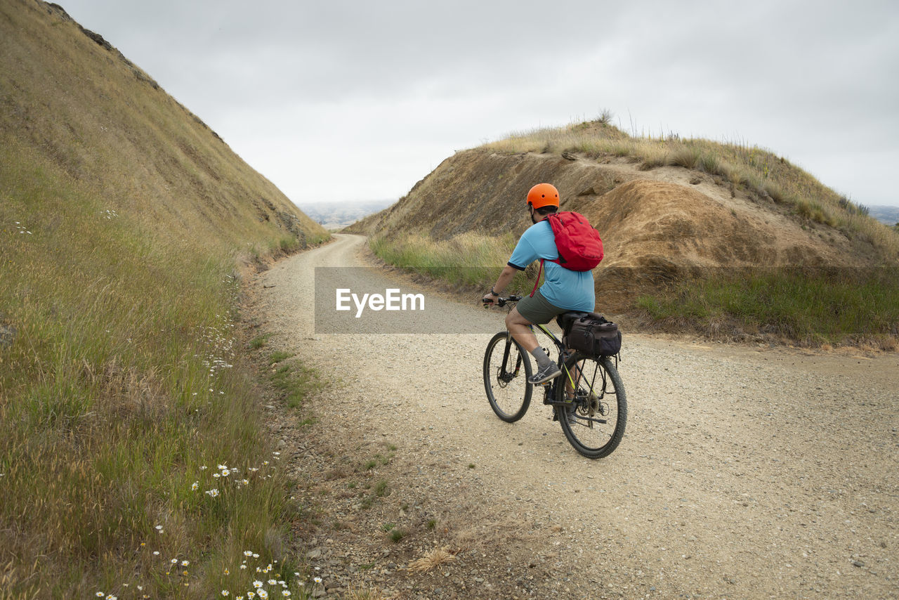 REAR VIEW OF WOMAN RIDING BICYCLE ON ROAD