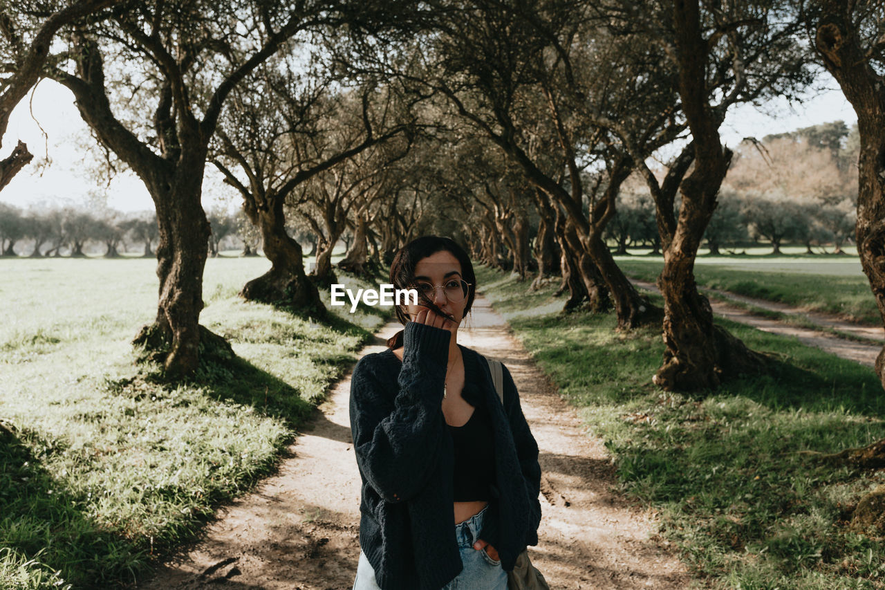 portrait of young woman standing against trees