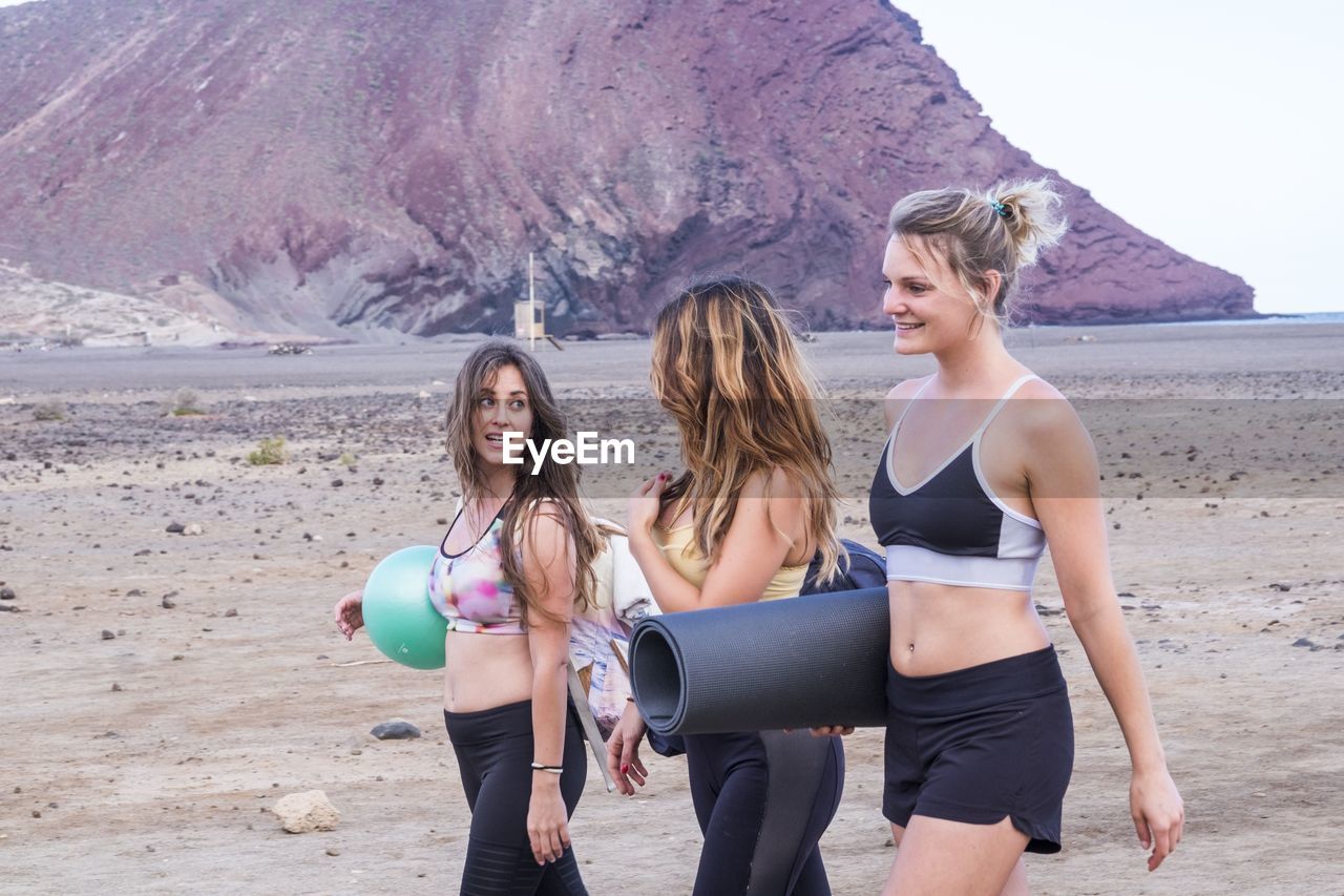 Smiling women carrying exercising mat on field