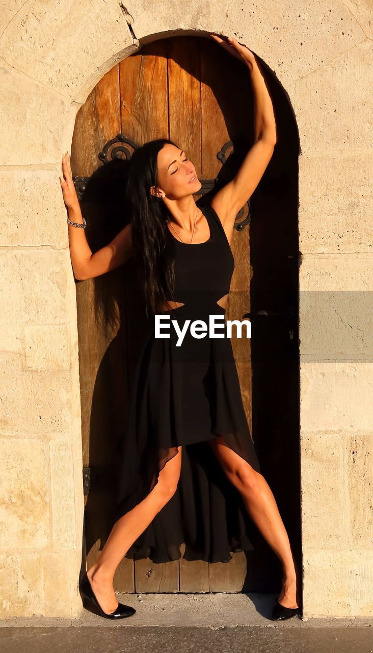 YOUNG WOMAN STANDING AGAINST WALL