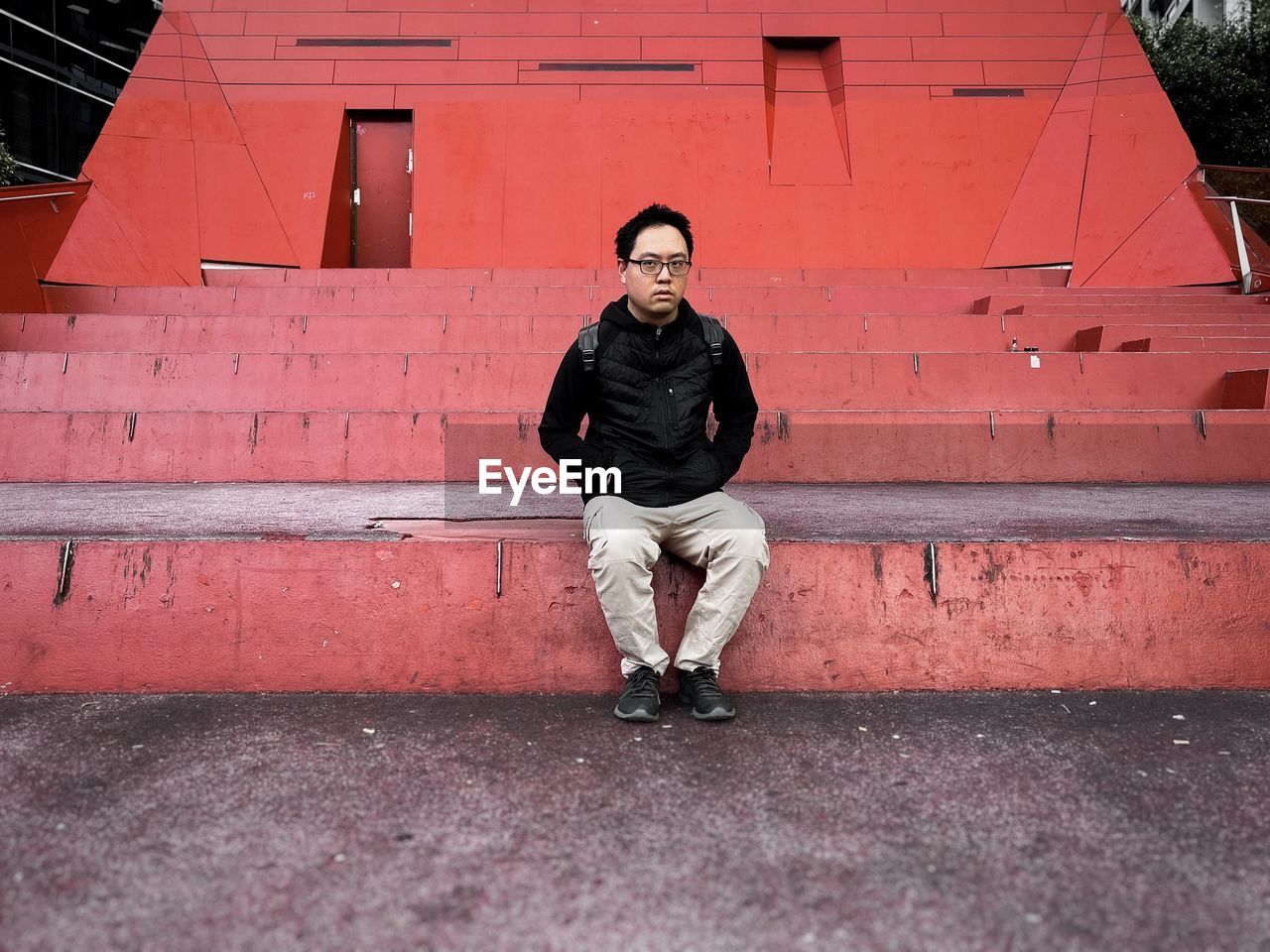 Asian man sitting on steps against orange wall and architecture.