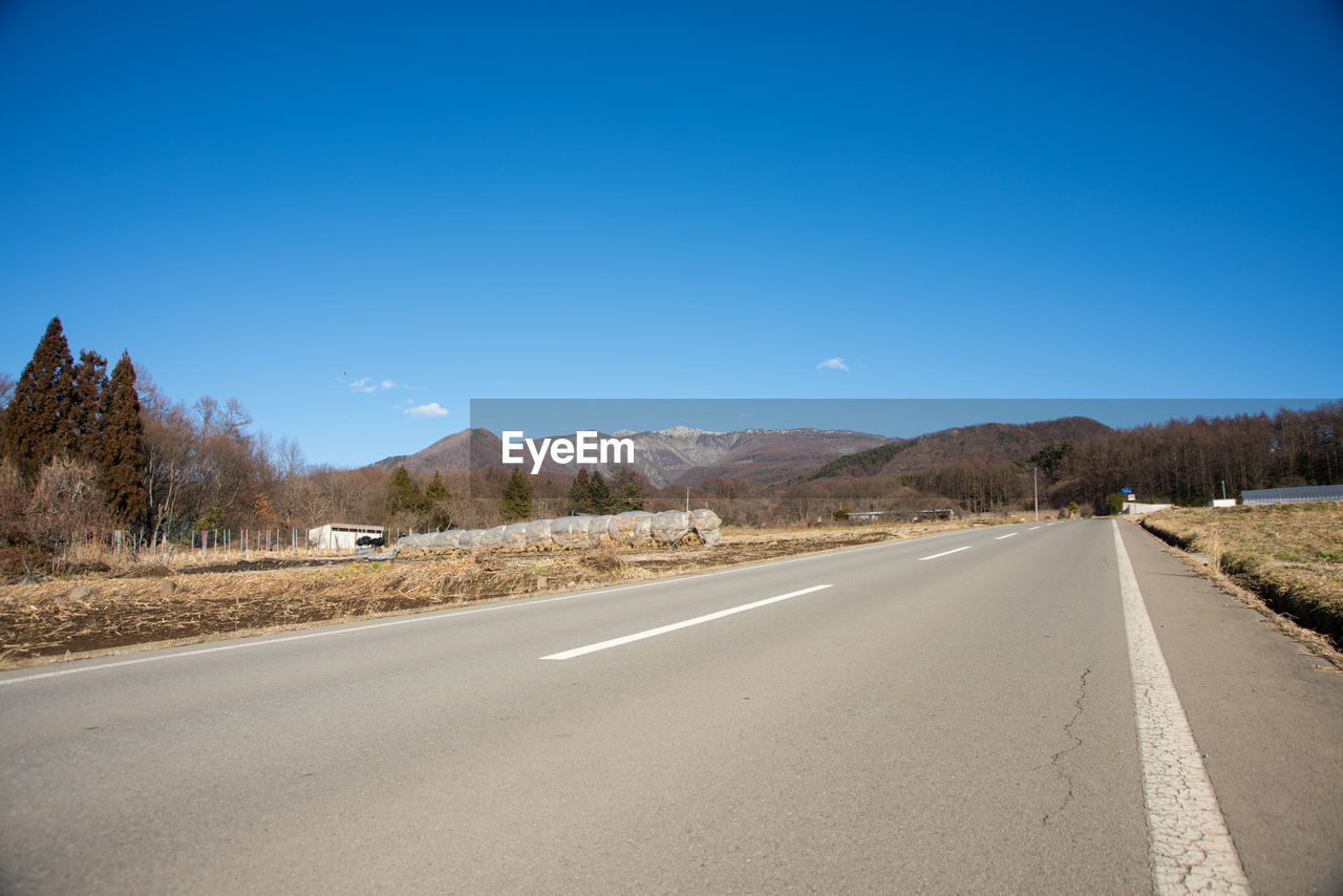 Road passing through landscape against clear blue sky