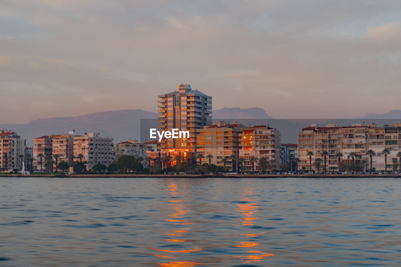 Sea by buildings against sky during sunset