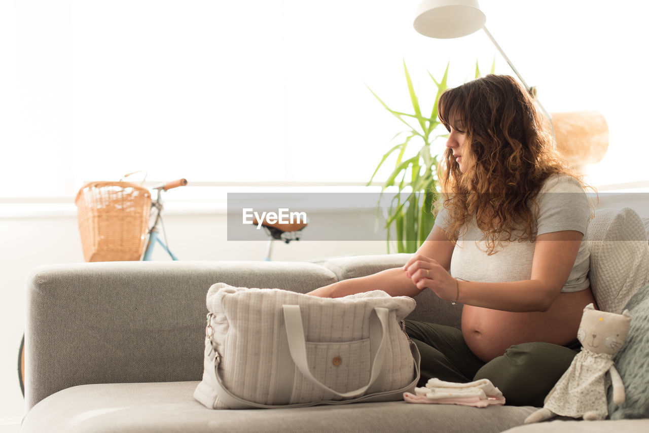 YOUNG WOMAN SITTING ON SOFA IN LIVING ROOM