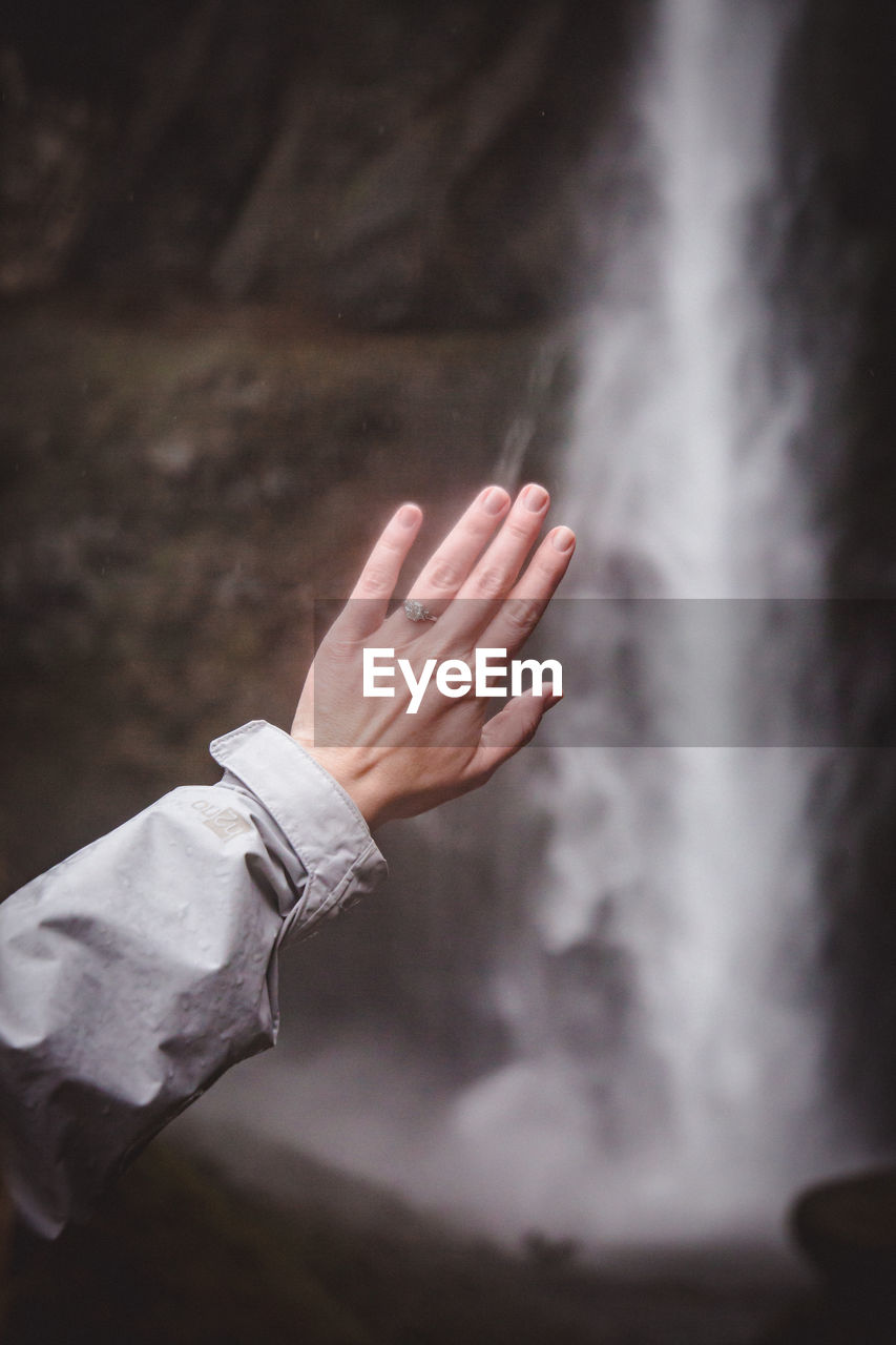 Close-up of hand against waterfall