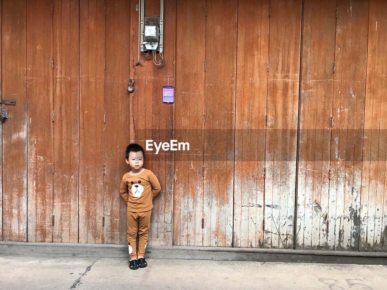 Boy standing against wooden wall