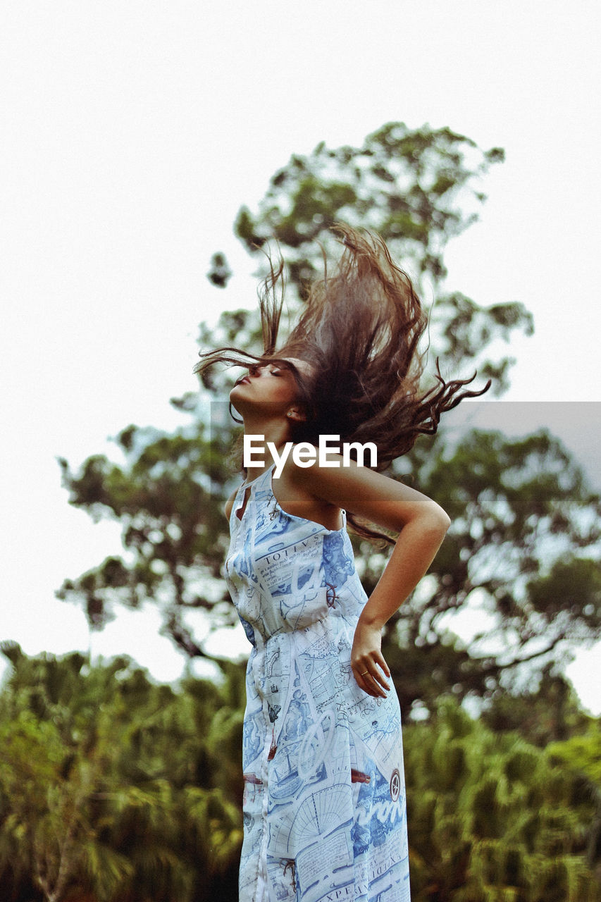 Low angle view of woman tossing hair against clear sky