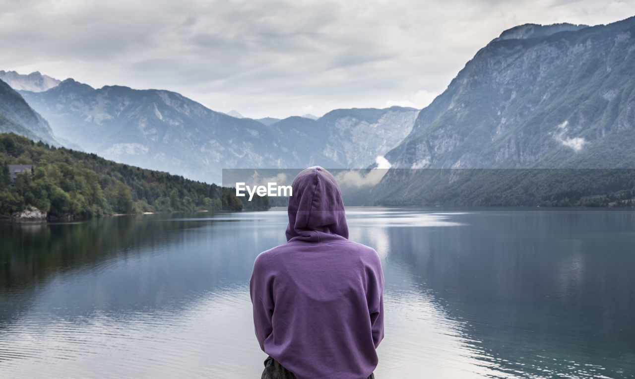 REAR VIEW OF WOMAN LOOKING AT LAKE AGAINST MOUNTAINS