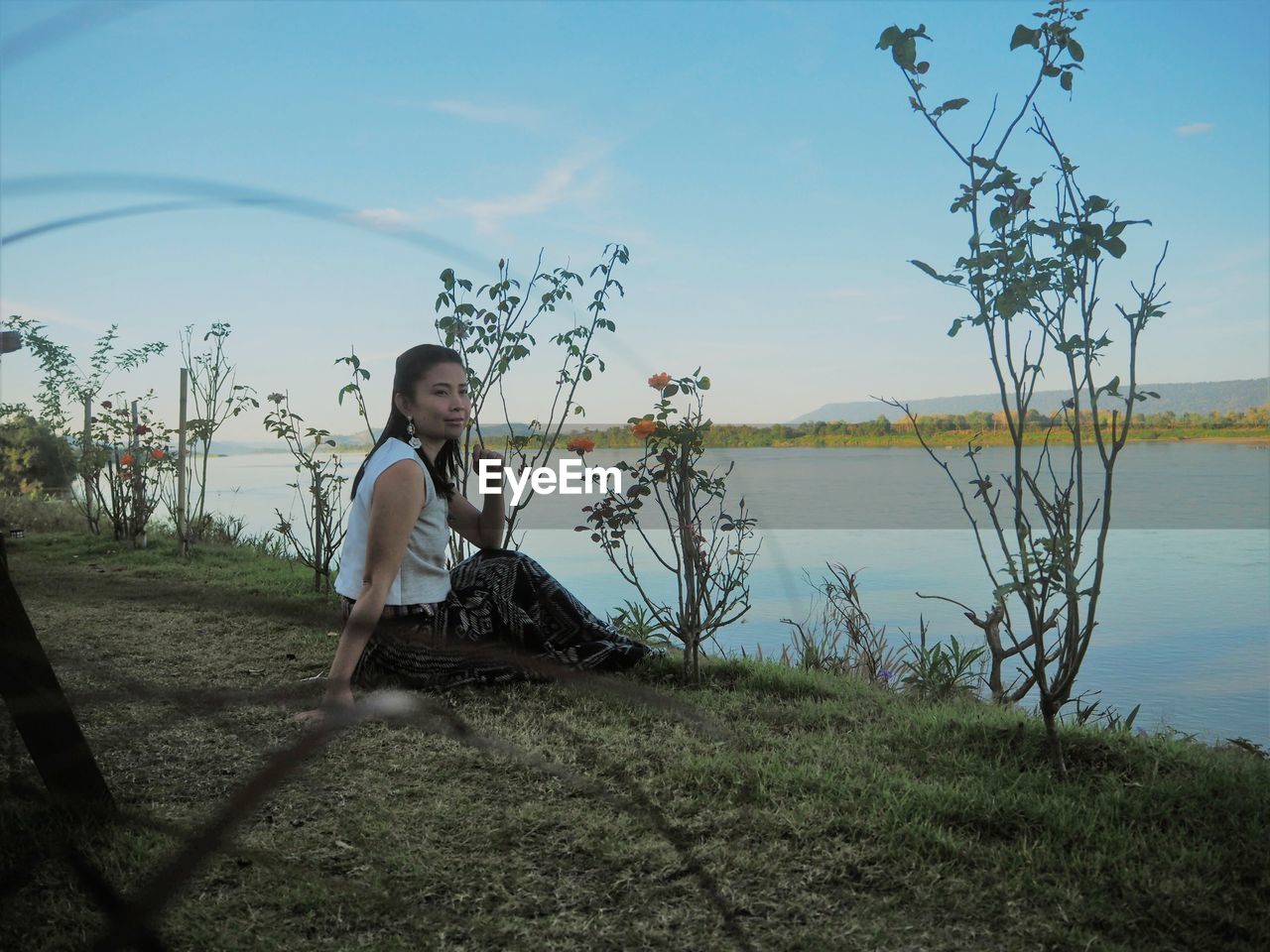 Woman looking away while sitting by lake against sky