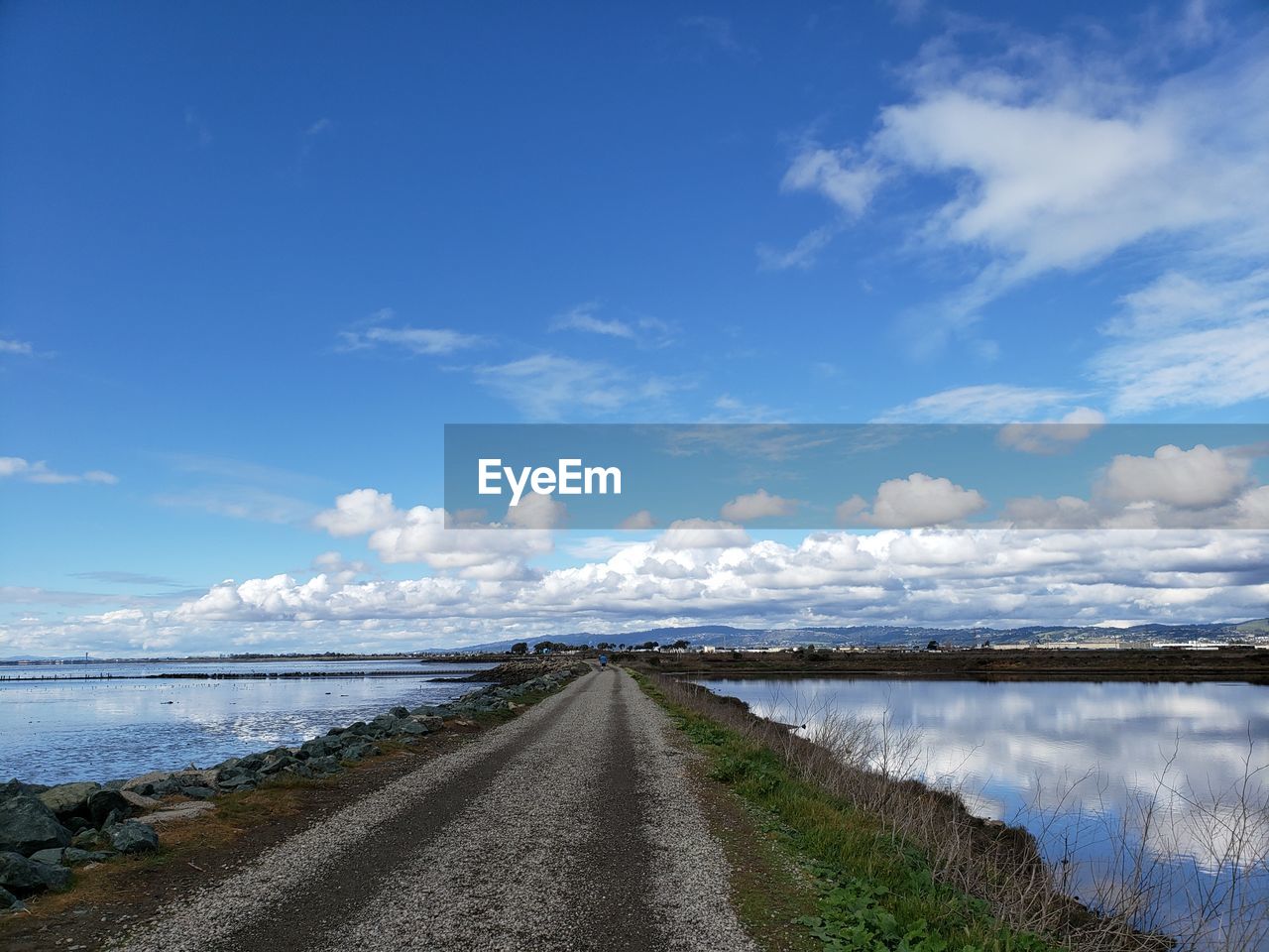 Empty road along calm sea against sky