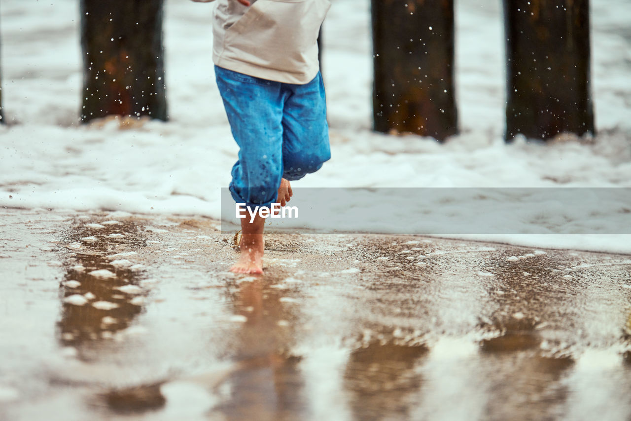 Little boy in blue pants running on sea coast and playing with sea waves, unfocused blurred legs