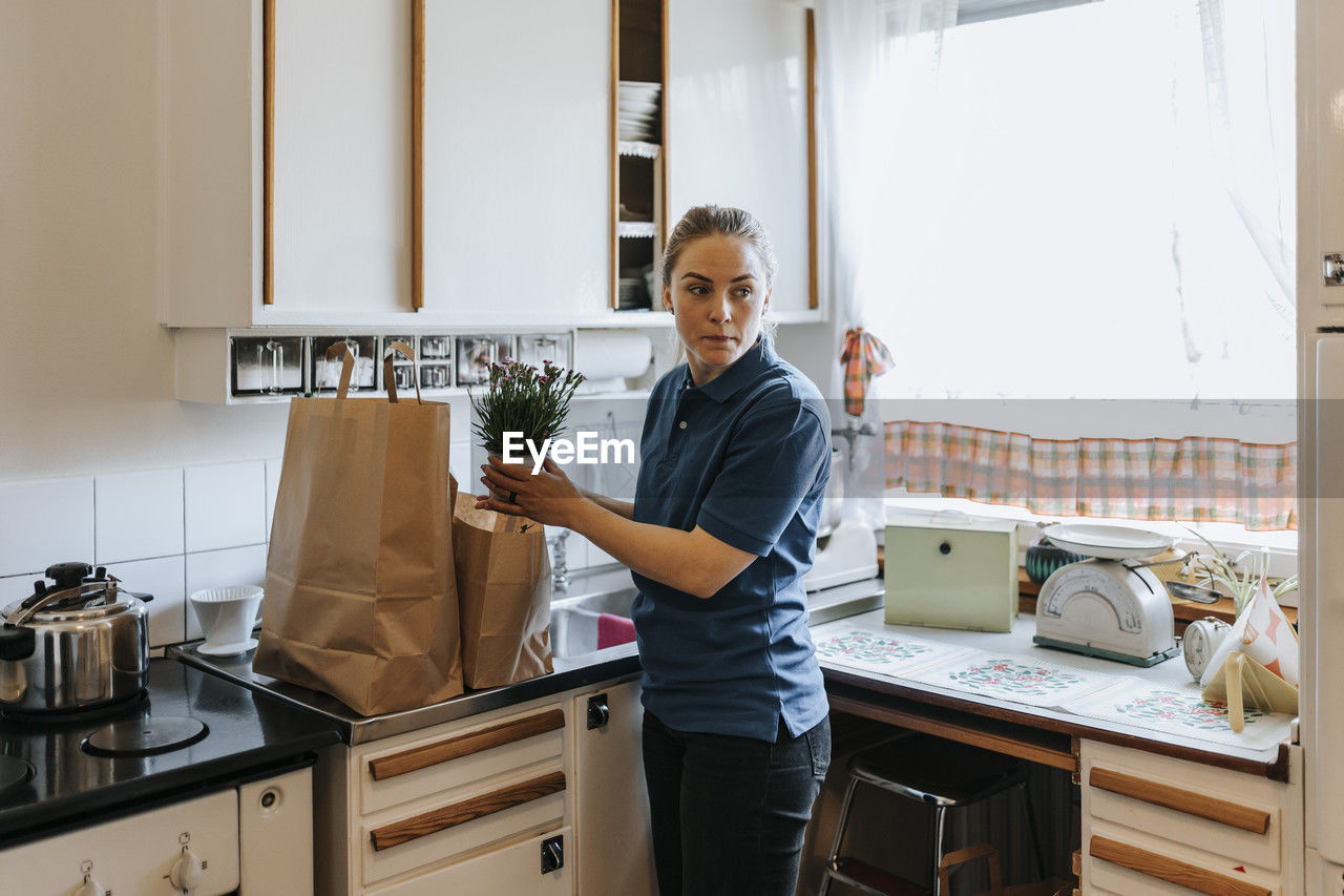 Female care assistant removing potted plant while standing in kitchen at home