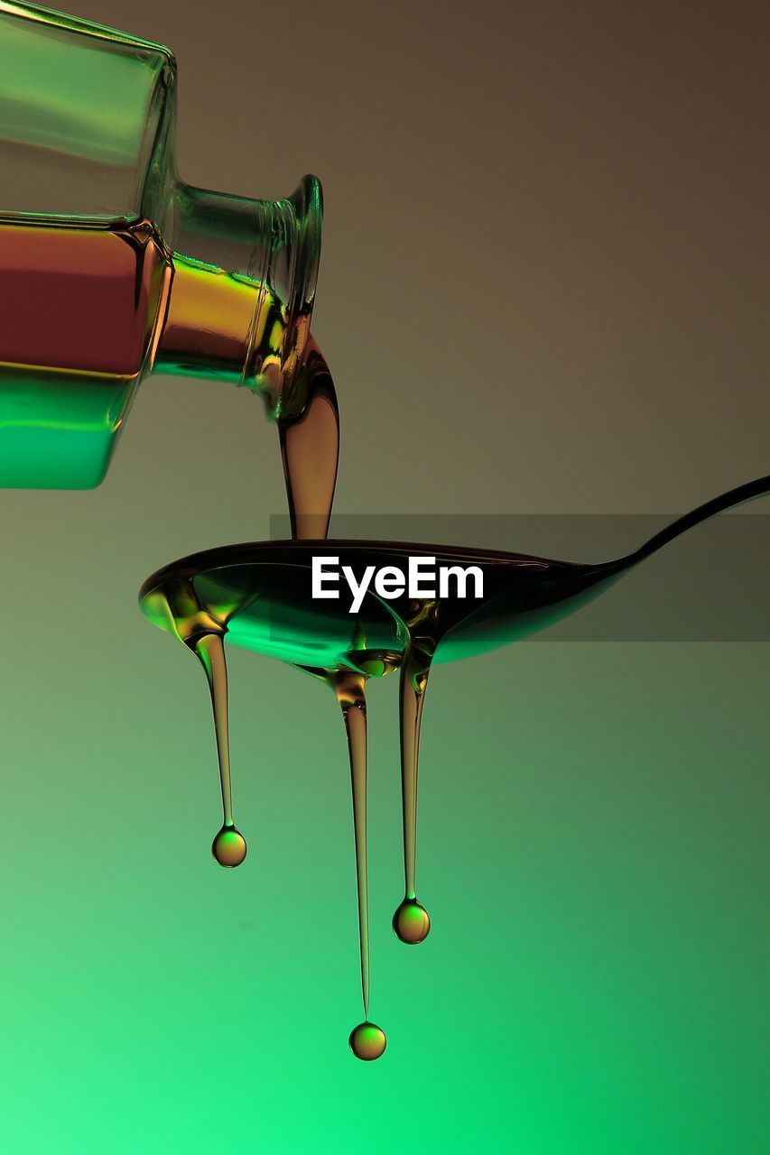 Close-up of oil pouring in spoon against colored background