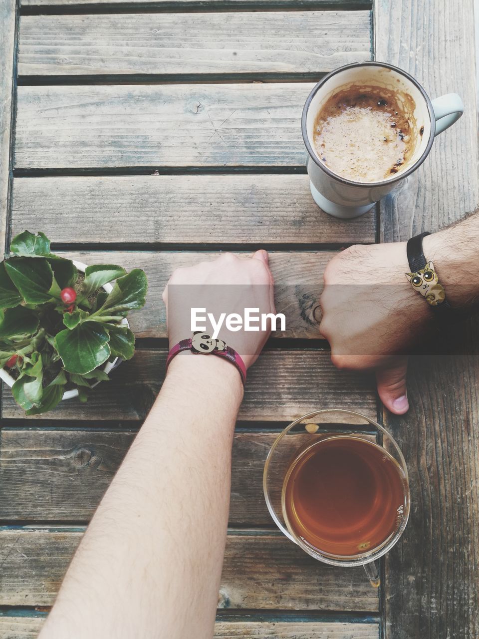 Close-up of people hands wearing bracelets by drinks on wooden table
